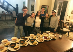 Group of students standing over a table of soup and sandwiches